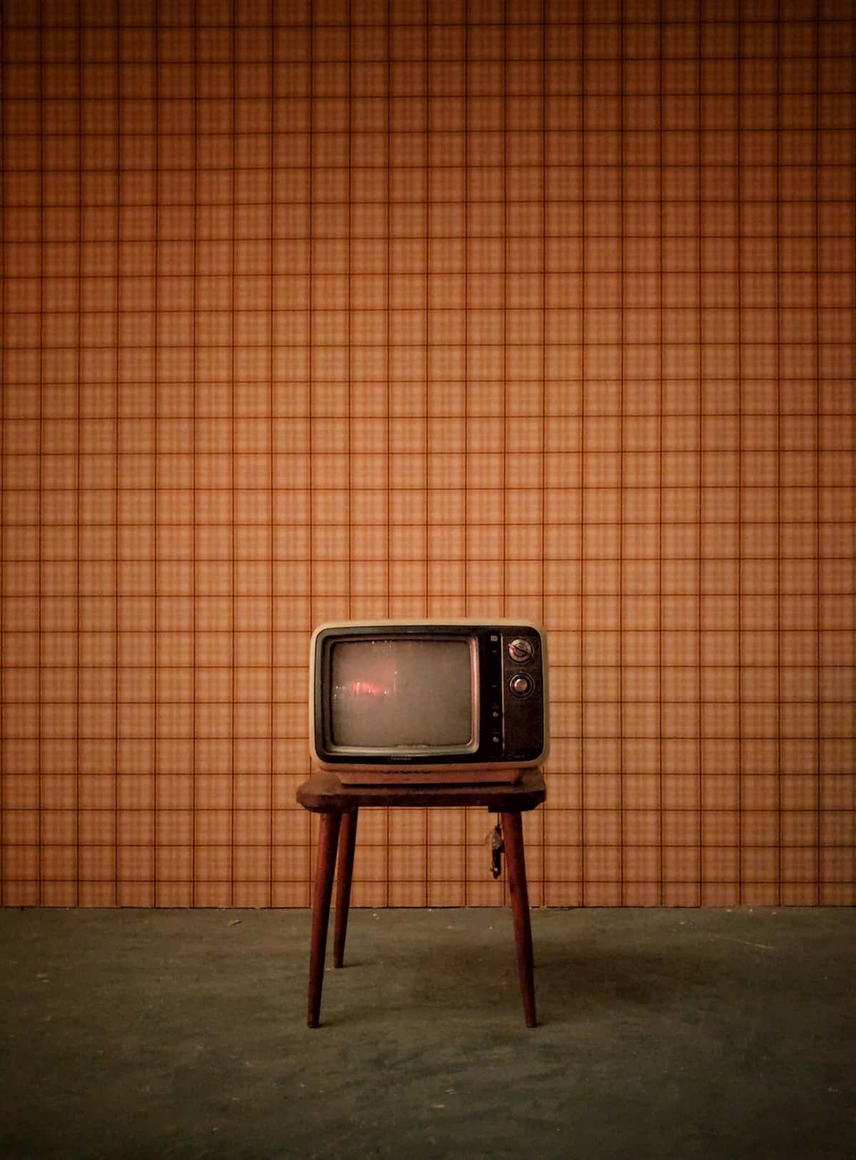 Kleine retrotelevisie op een krukje voor een oranje muur