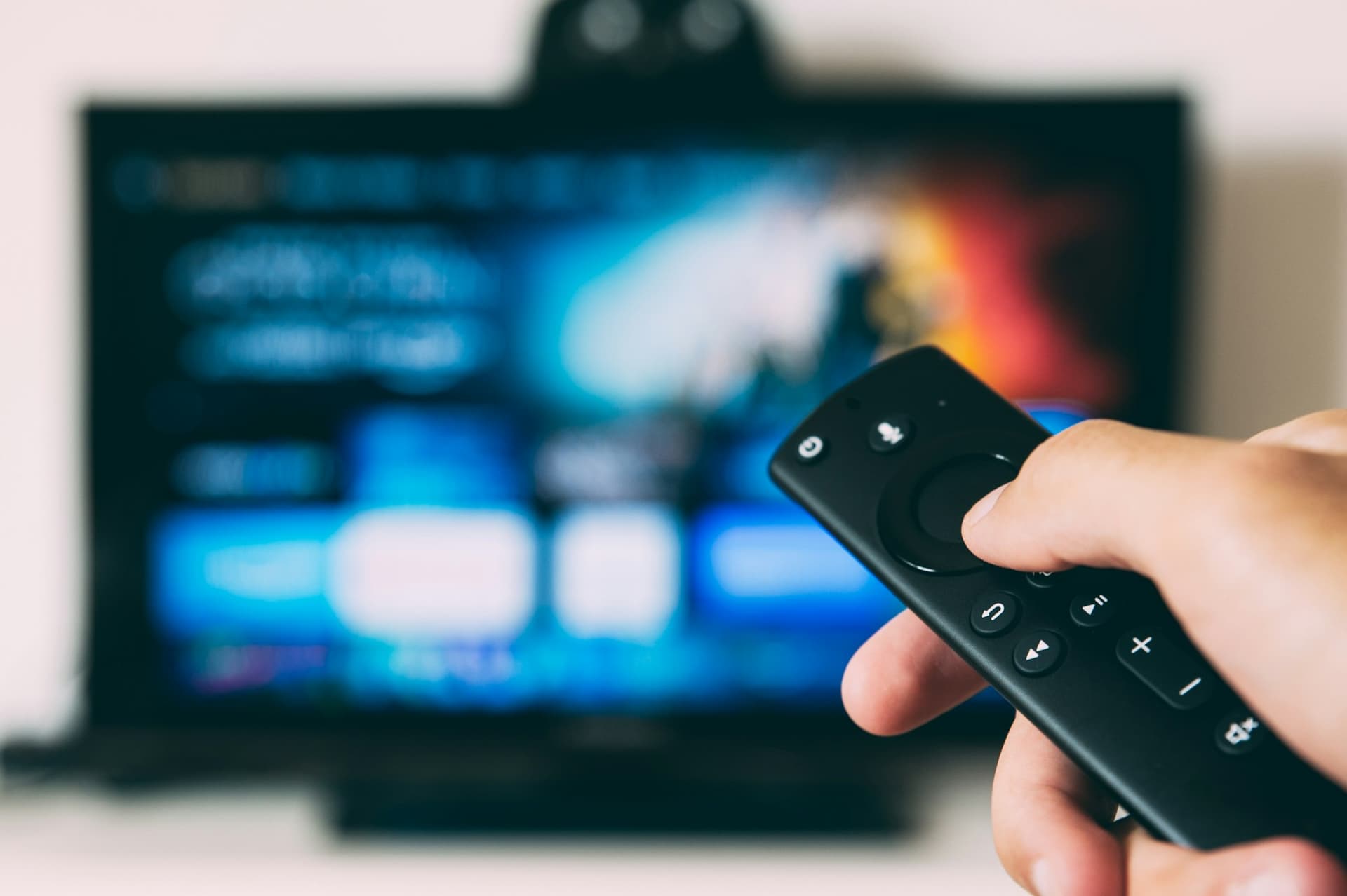 Hand met afstandsbediening gericht op een televisie in een donkere woonkamer